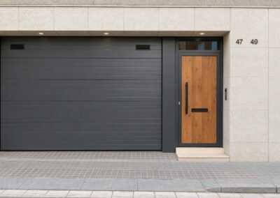Fachada vivienda con garaje puerta plegable metálica y puerta mixta acero y madera.